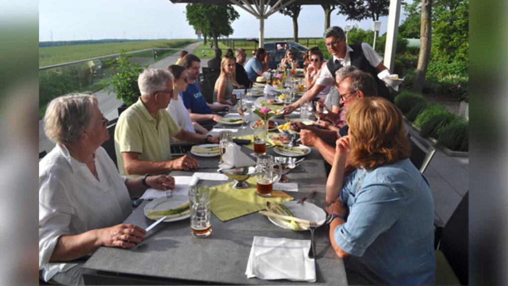 Teilnehmende der Coesfelder Genusswanderung sitzen gemeinsam an einer langen Tafel im Freien