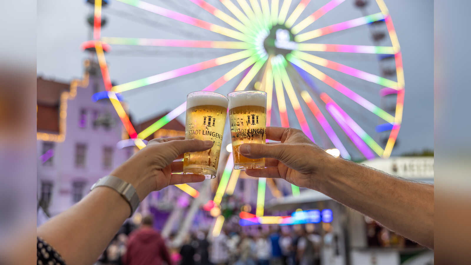 Zwei Besucher stoßen mit Bier vor dem beleuchteten Riesenrad beim Lingener Altstadtfest an