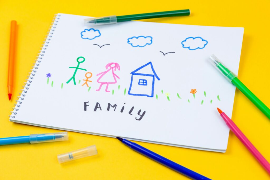 Filzstift liegt auf einer bunten Kinderzeichnung, die eine Familie zeigt