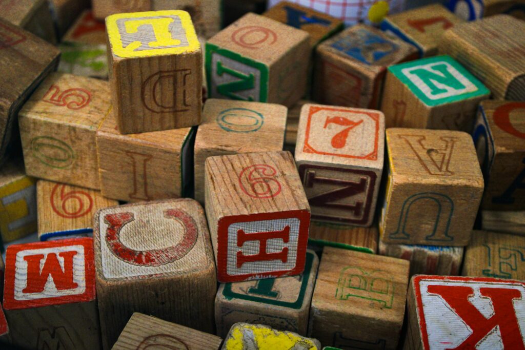 Bunte Holzbuchstaben-Bausteine aufgestapelt (Symbolbild)