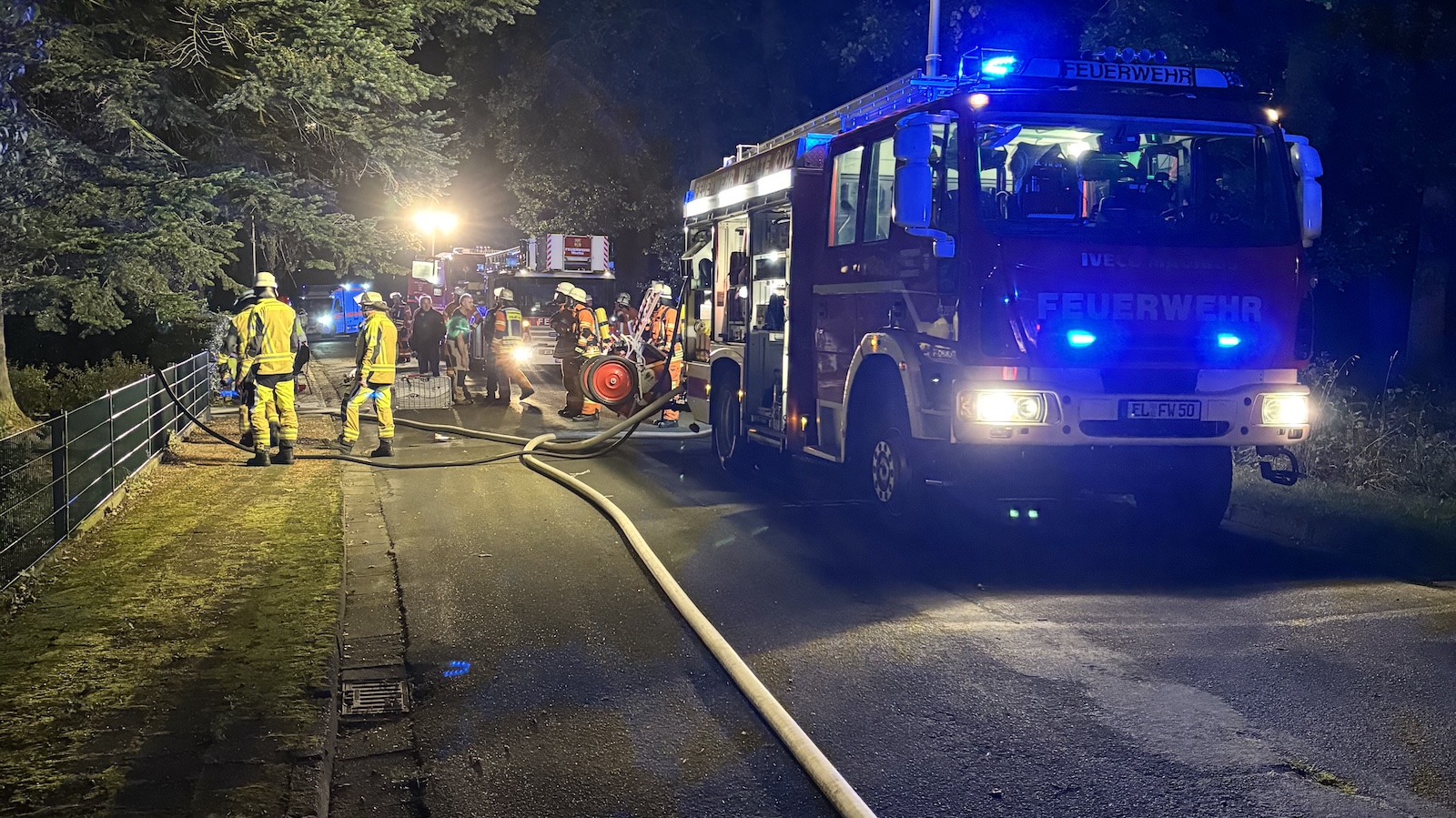 Einsatzkräfte der Feuerwehr vor einem Einfamilienhaus in Werlte, aus dessen Fenster Flammen schlagen