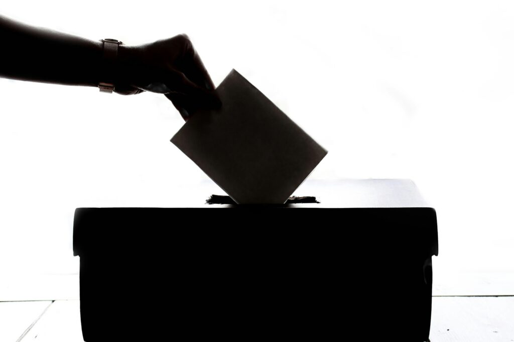 Eine Hand wirft einen Stimmzettel in eine Wahlurne