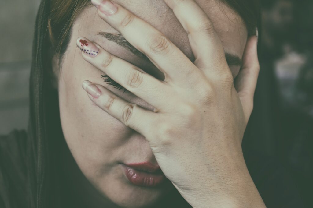 Frau hält sich schmerzbedingt die Hand ans Gesicht, Symbolbild für Migräne und Kopfschmerz