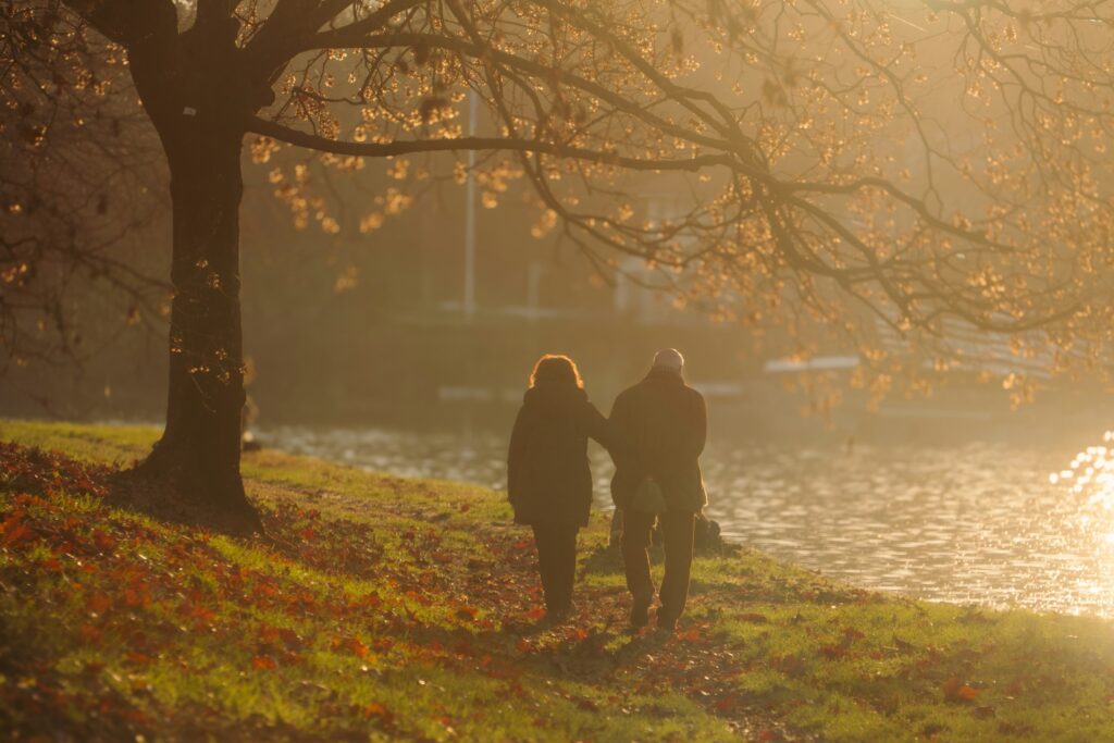 Älteres Paar spaziert bei Sonnenuntergang an einem Fluss entlang (Symbolbild)
