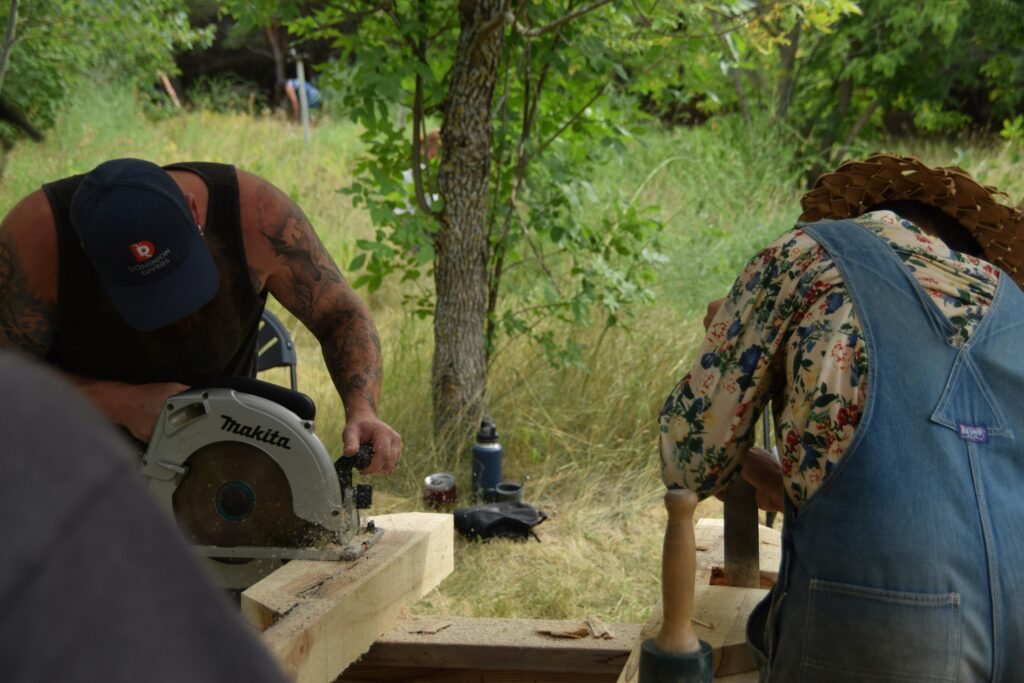 Zwei Handwerker sägen und bearbeiten Holzbalken im Freien
