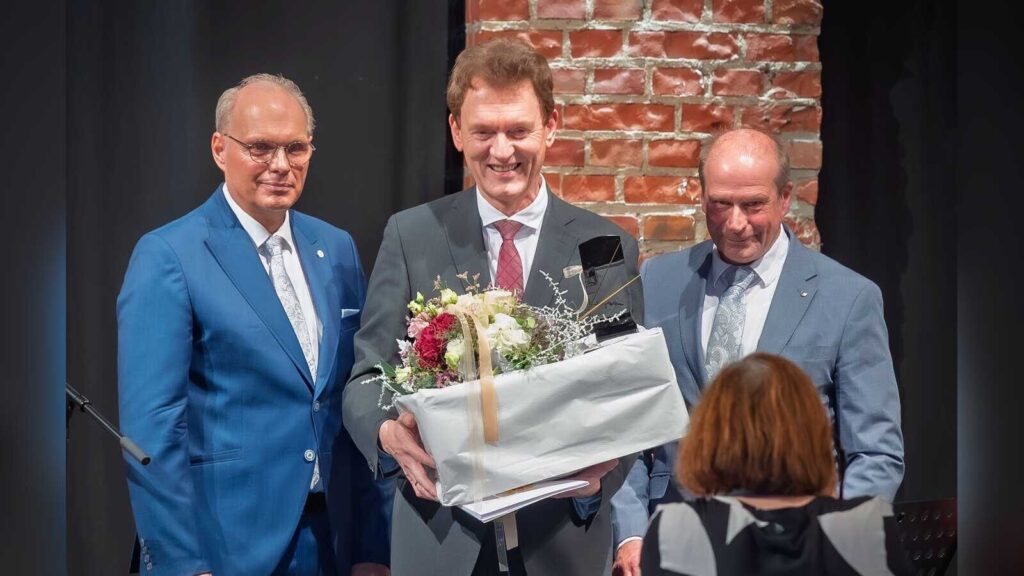 Dieter Krone mit Blumenstrauß und Geschenk zwischen Stefan Heskamp und Lothar Schreinemacher auf der Bühne der Halle IV