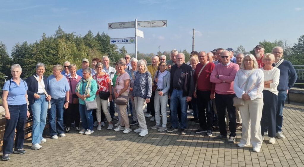 Gruppenfoto der Lingener Reisegruppe im Freien an einem Wegweiser mit Richtungsschildern nach Lingen und Hronov