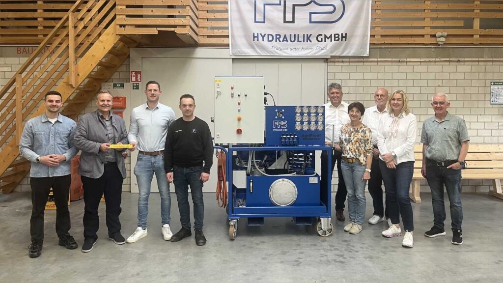 Gruppe aus Gemeindevertretern und Firmeninhabern in einer Werkshalle neben einem blauen Hydraulikaggregat, darüber ein Banner der FPS Hydraulik GmbH