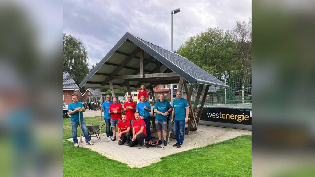 Rund ein Dutzend Helferinnen und Helfer in roten und blauen T-Shirts vor dem neuen Unterstand am Bouleplatz des FC Wesuwe