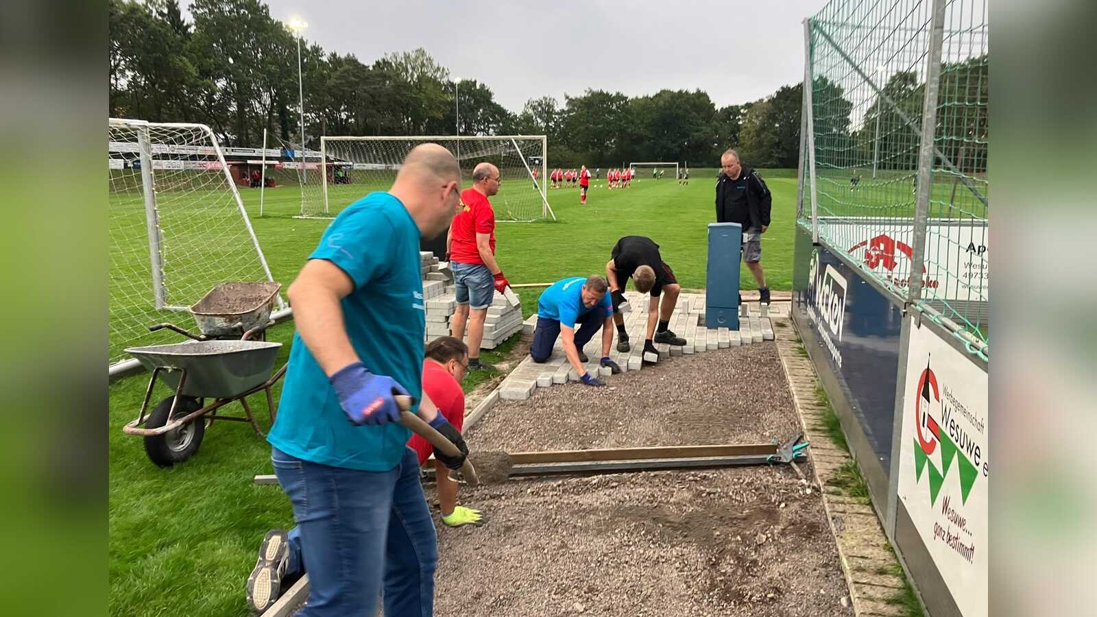 Helfer verlegen Pflastersteine am Rand des neuen Bouleplatzes, im Hintergrund Fußballtore auf dem Vereinsgelände