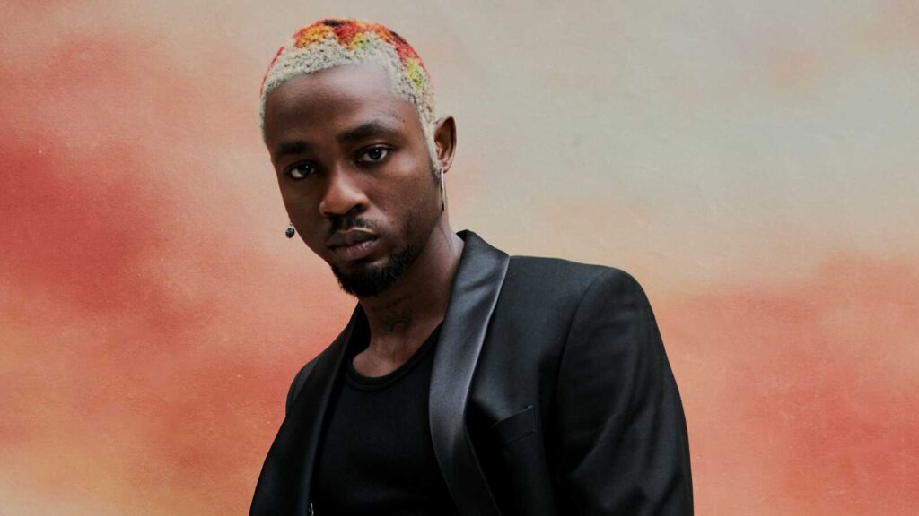 Musiker Omah Lay mit gebleichten, bunt gefärbten kurzen Haaren und schwarzem Sakko