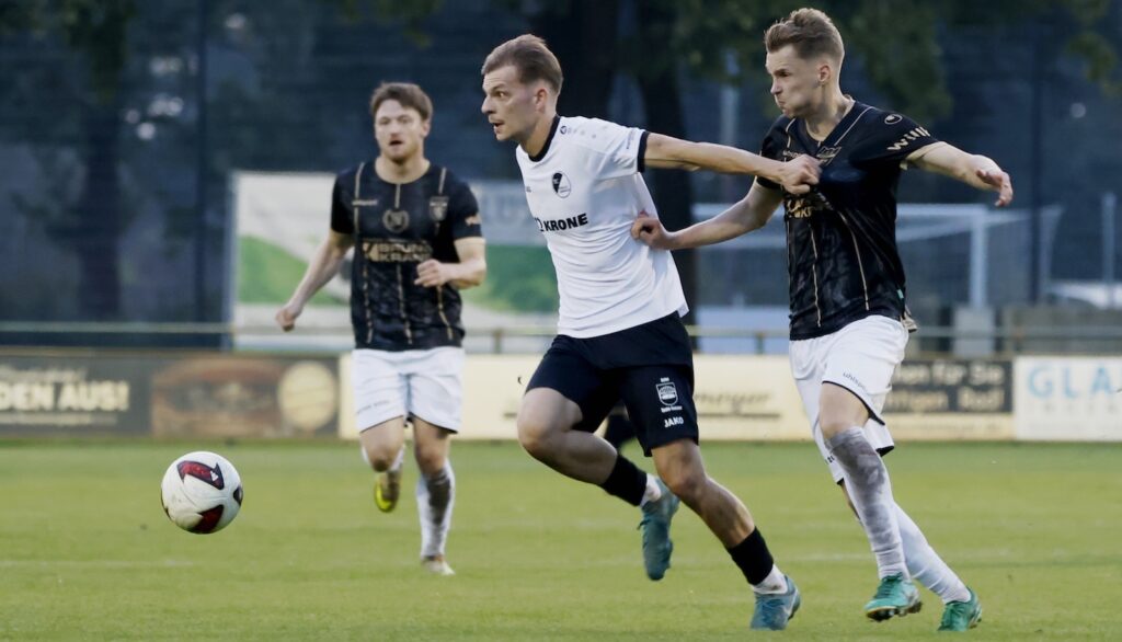 Adrian Lenz vom SC Spelle-Venhaus im weißen Trikot setzt sich im Zweikampf gegen einen Gegenspieler in Schwarz durch