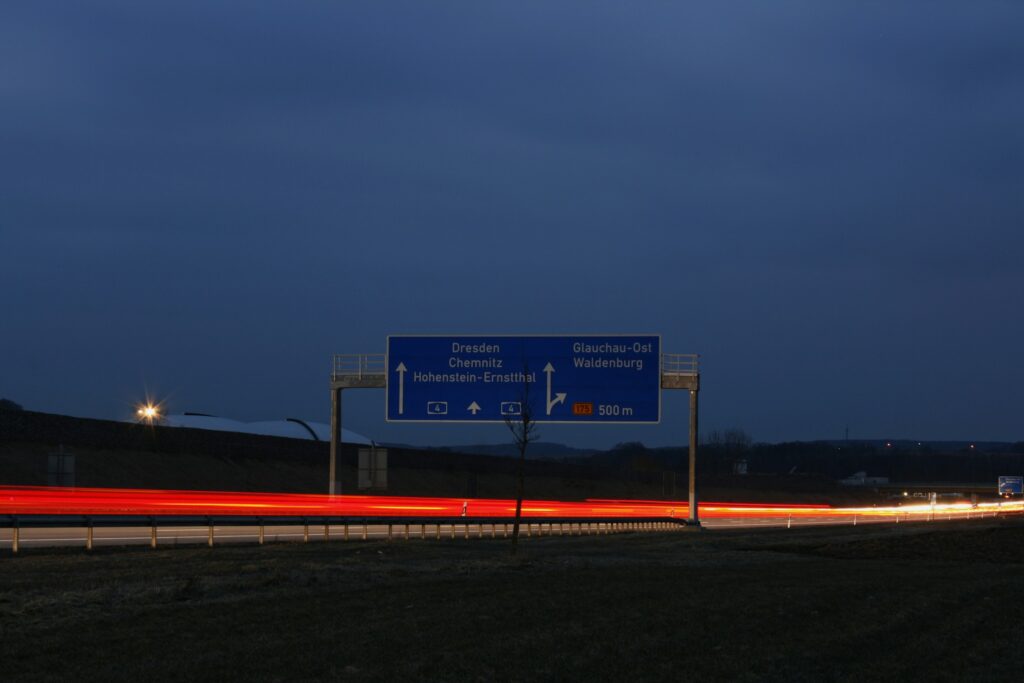 Autobahnschild bei Nacht mit Lichtspuren vorbeifahrender Fahrzeuge