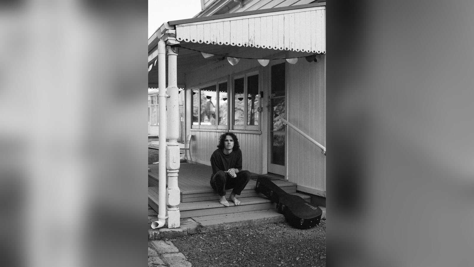 Schwarzweißfoto: Joseph G. Thompson sitzt barfuß auf den Stufen einer Holzveranda, neben ihm ein Gitarrenkoffer