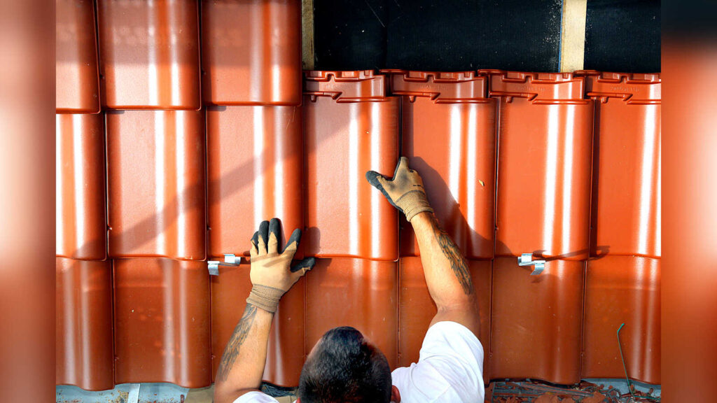Dachdecker verlegt Dachpfannen auf einem Steildach