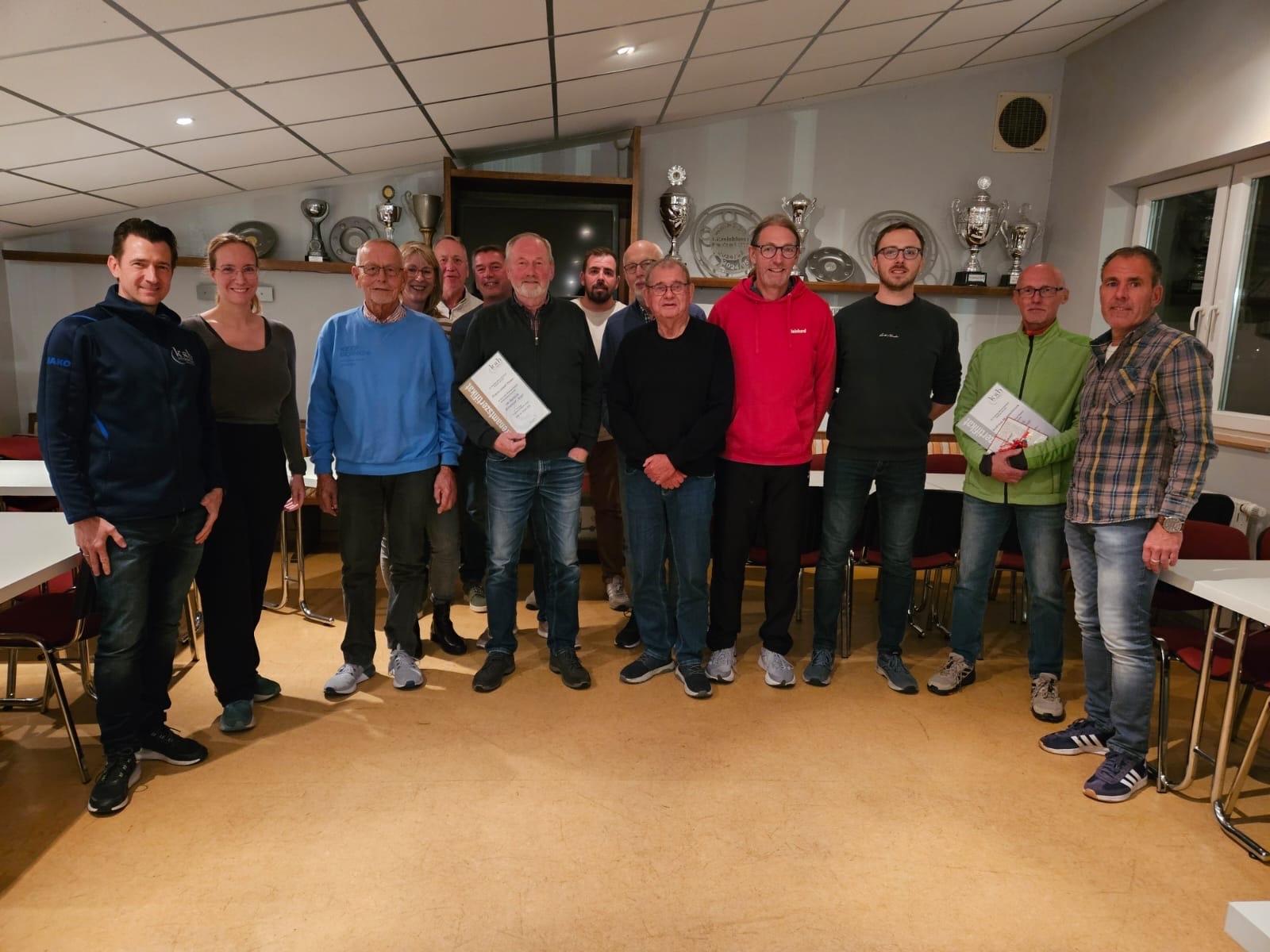 Gruppenfoto der Sportabzeichen-Prüfer in einem Vereinsraum mit Pokalen im Regal