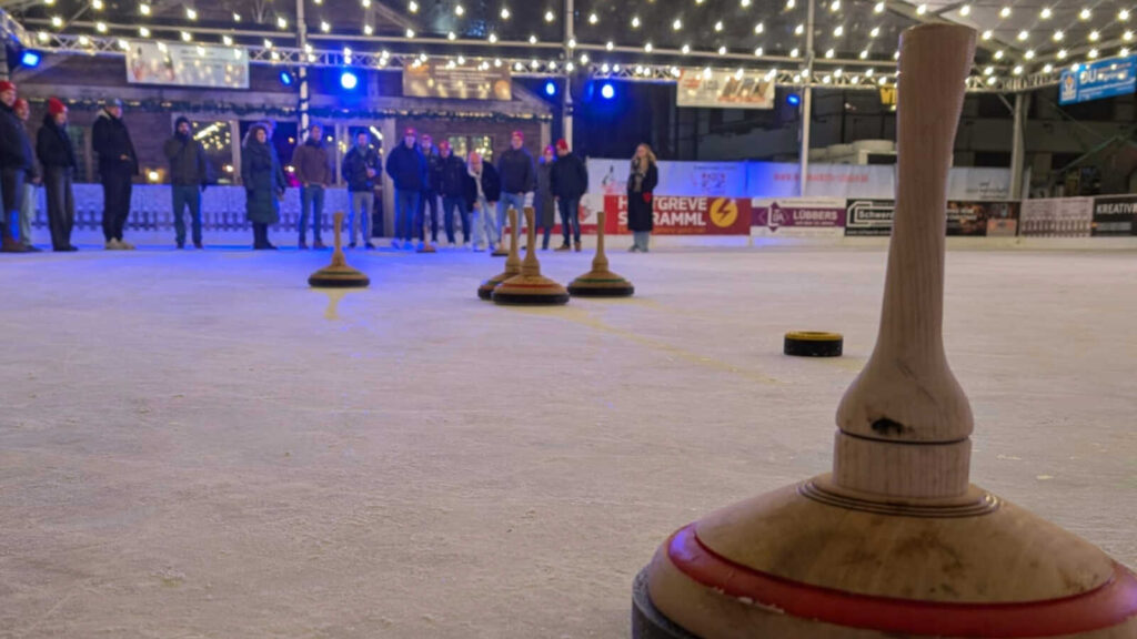 Eisstock im Vordergrund auf der überdachten Eisbahn des Lingener Weihnachtsmarktes, dahinter wartende Spieler