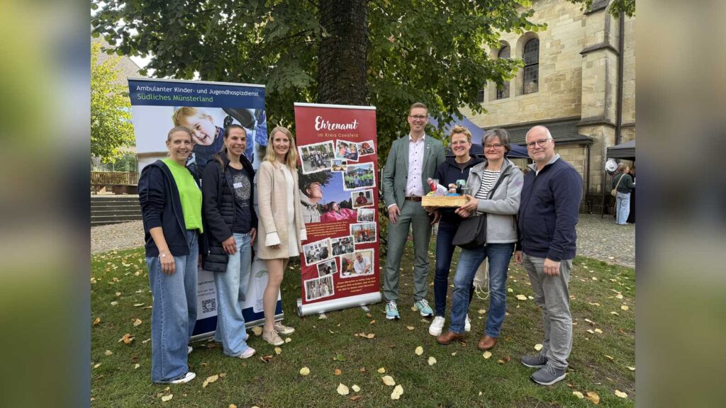 Bürgermeister Carsten Hövekamp übergibt einen Präsentkorb an Hilla Berheide sowie Leonie und Andreas Steens vor dem Banner mit dem prämierten Foto