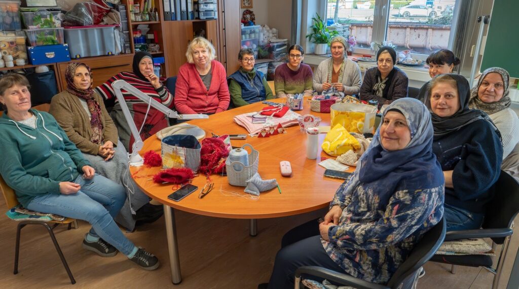 Frauen sitzen um einen runden Tisch mit Strickzeug, Wolle und genähten Taschen