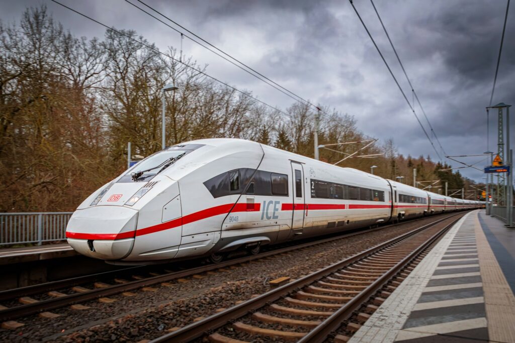 ICE-Hochgeschwindigkeitszug der Deutschen Bahn fährt bei bewölktem Himmel über eine Bahnstrecke