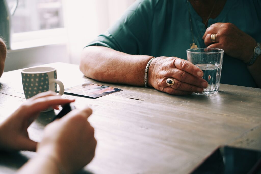 Ältere Frau und Familie sitzen bei Kaffee zusammen am Tisch und unterhalten sich