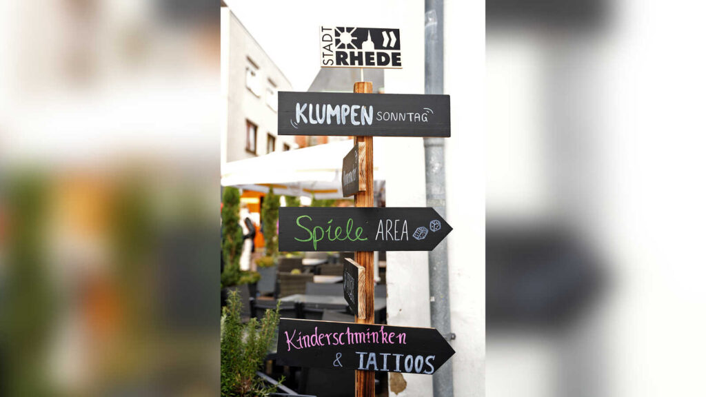 Holzwegweiser mit Schildern Klumpensonntag, Spiele-Area und Kinderschminken in der Rheder Innenstadt