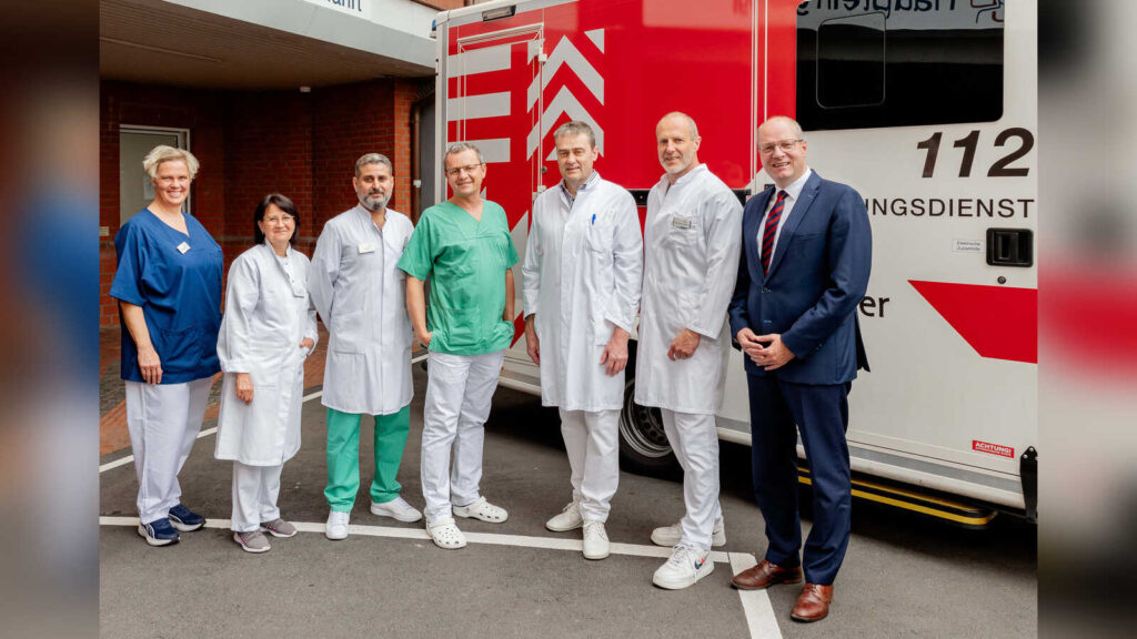 Sieben Ärzte, Pflegekräfte und der Geschäftsführer des Krankenhauses Damme stehen vor einem Rettungswagen