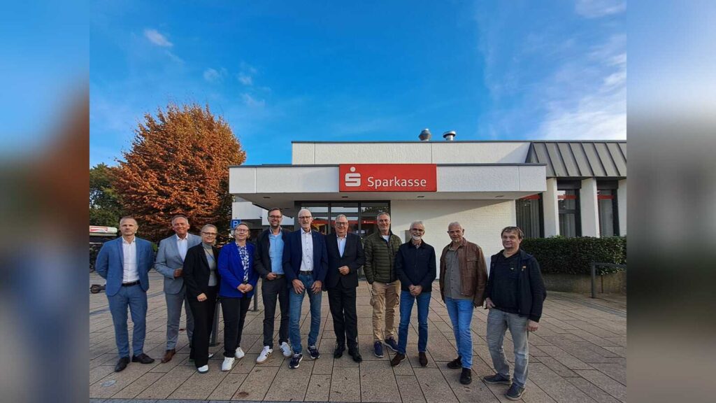 Vertreter der Gemeinde Belm und der Sparkasse Osnabrück stehen vor der Sparkassenfiliale am Marktring in Belm