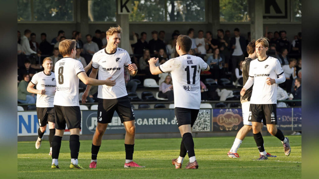 Spieler des SC Spelle-Venhaus in weißen Trikots klatschen sich nach einem Tor gegen den Lüneburger SK Hansa ab, im Hintergrund die Tribüne