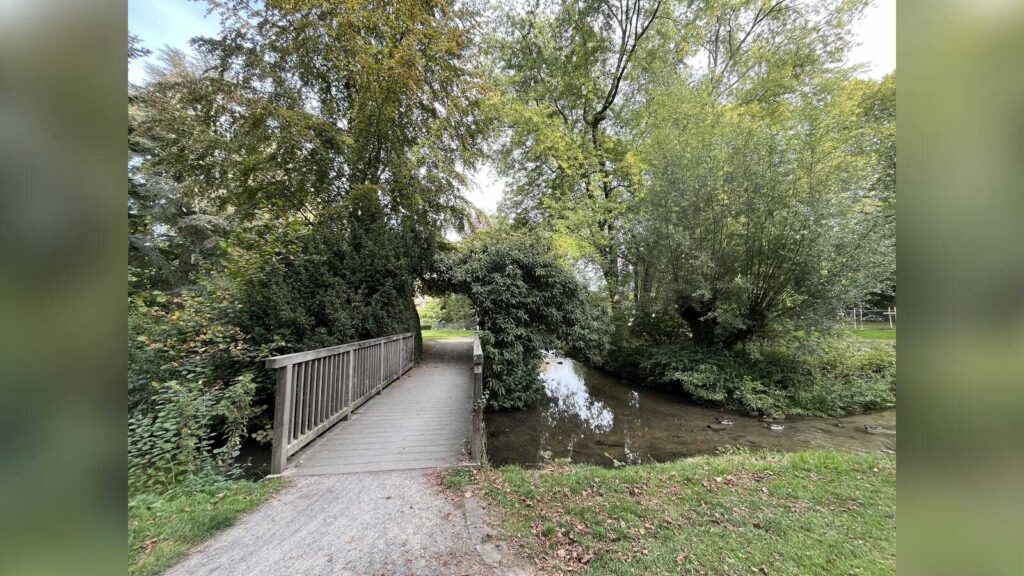 Holzbrücke mit Geländer über den Honigbach im Coesfelder Stadtpark, umgeben von Bäumen und Büschen