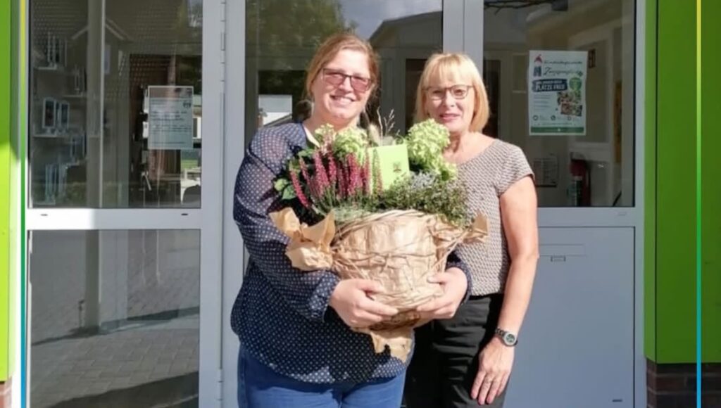 Zwei Frauen vor dem Eingang der Kita Zwergenglück in Surwold, eine hält einen großen Blumentopf mit Heide und Hortensien