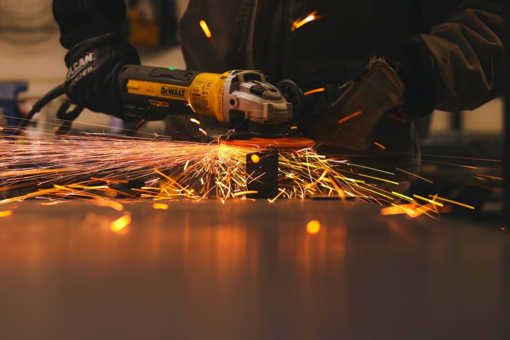 Ein Mann bearbeitet in einer Werkstatt ein Metallteil mit einem Winkelschleifer, Funken sprühen