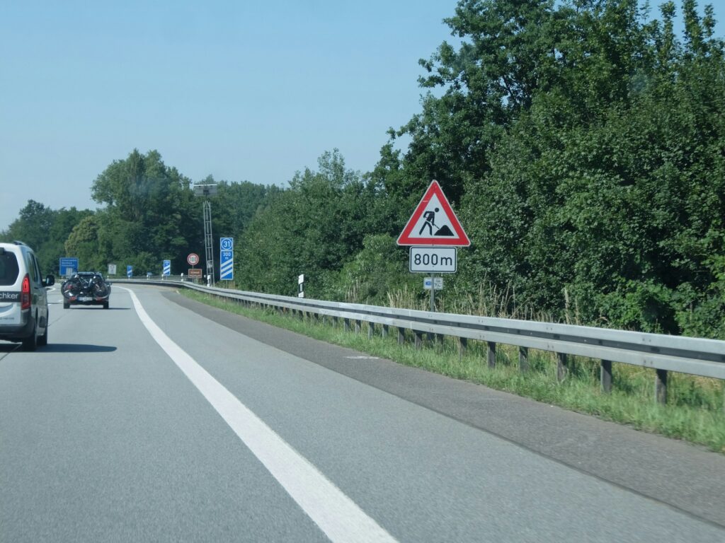Landstraße mit Baustellen-Warnschild und Leitplanke