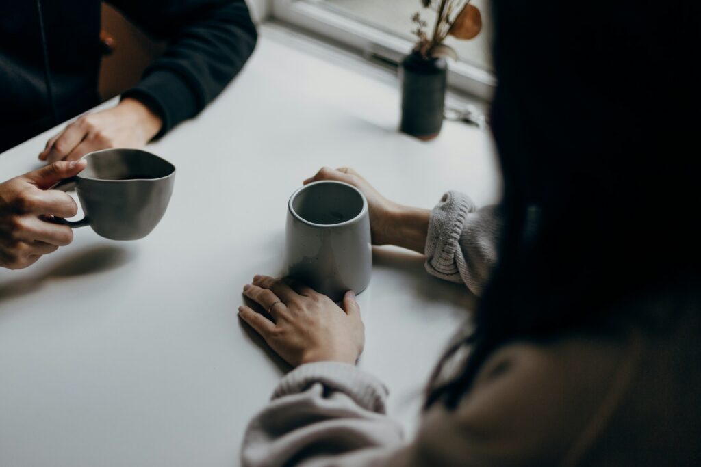 Zwei Personen mit Kaffeebechern im Gespräch an einem Tisch, Symbolbild für Streitschlichtung