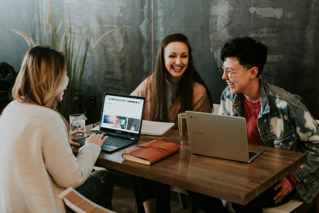 Mehrere Menschen sitzen mit Laptops an einem Tisch und tauschen sich aus