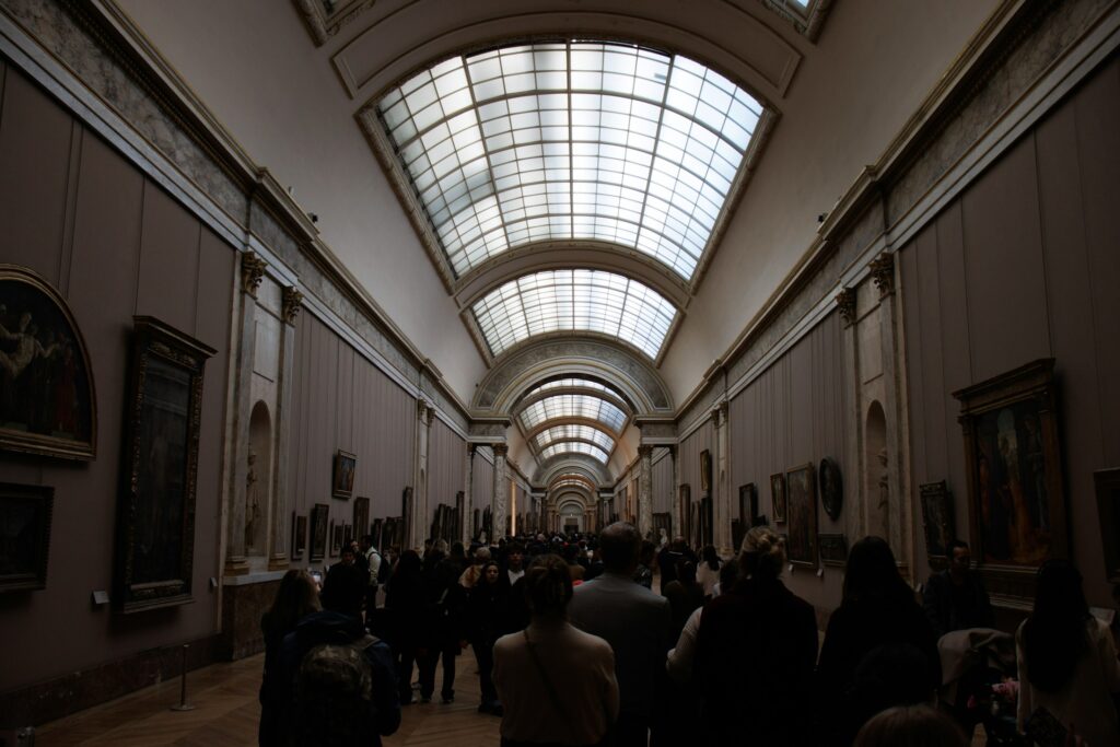 Besucherinnen und Besucher gehen durch eine lange Galerie mit Gemälden an den Wänden
