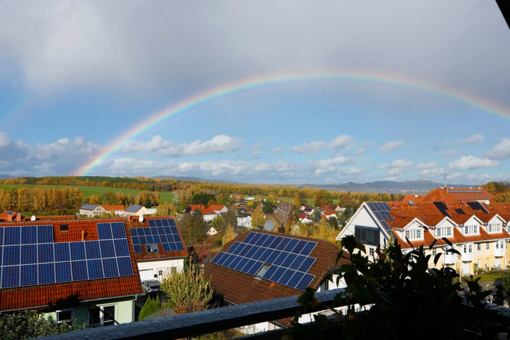 Mehrere Wohnhäuser mit Photovoltaikanlagen auf den Dächern, darüber ein Regenbogen