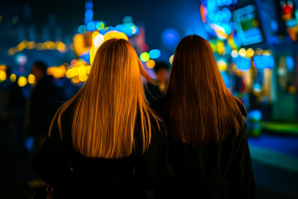 Zwei Frauen gehen abends durch eine beleuchtete Stadt