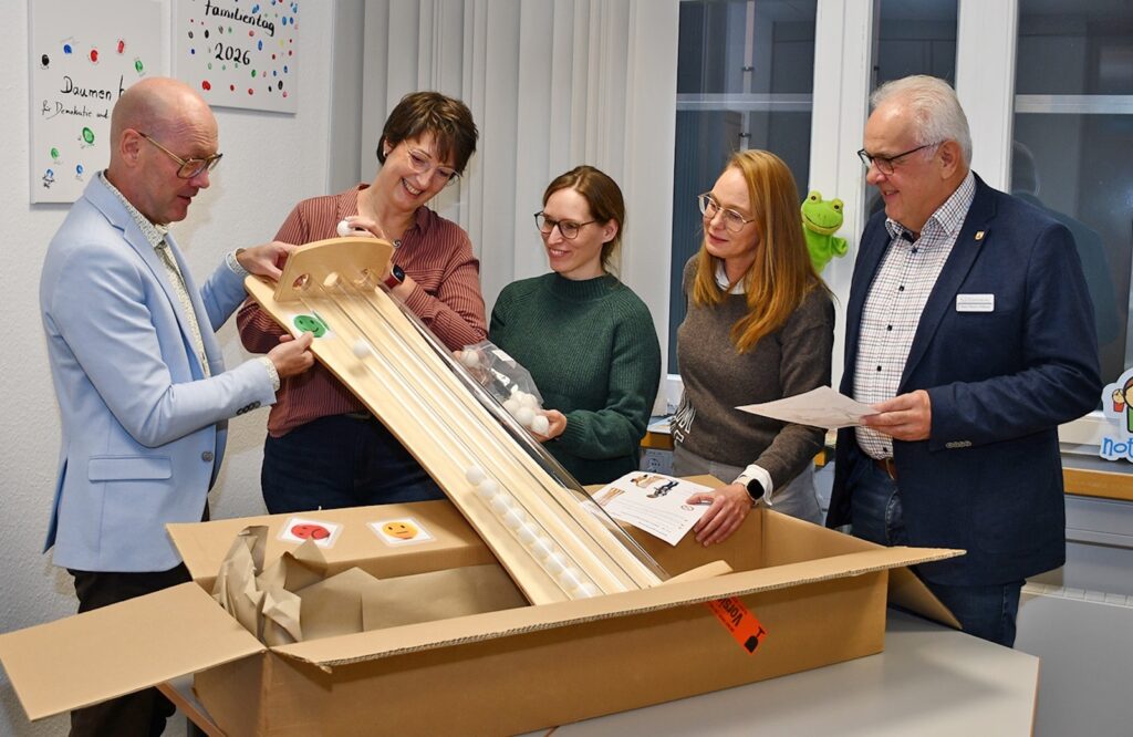 Fünf Personen packen eine hölzerne Abstimmungssäule mit Röhren aus einem Karton aus