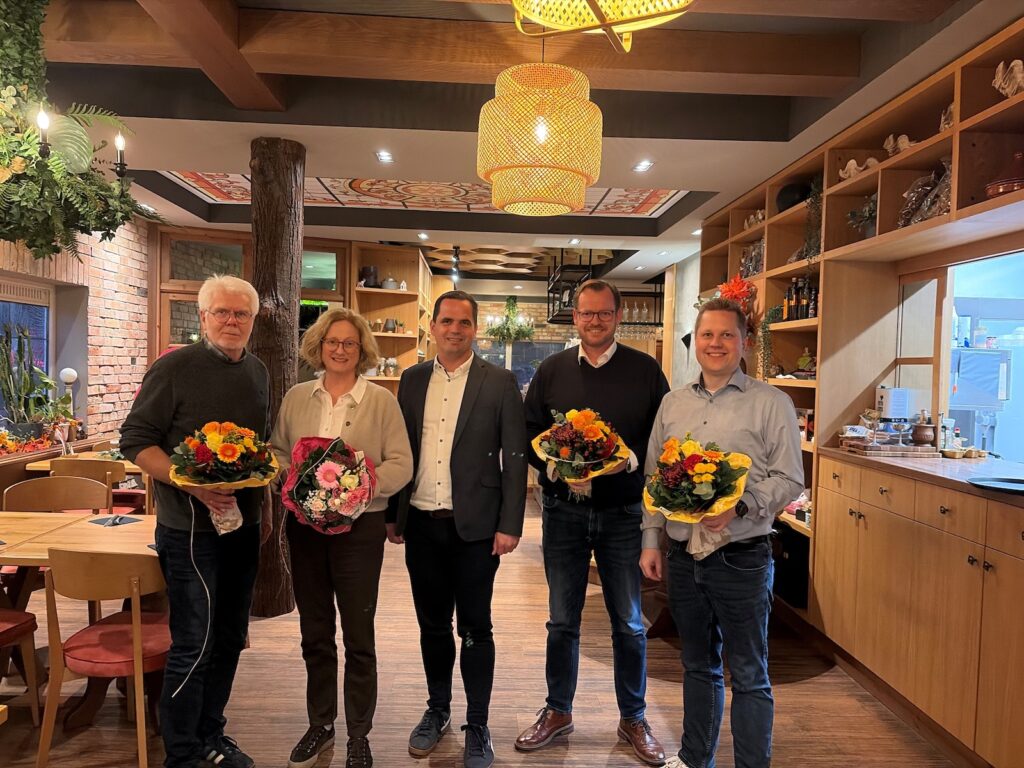 Fünf Personen stehen in einem Restaurant, vier von ihnen halten Blumensträuße