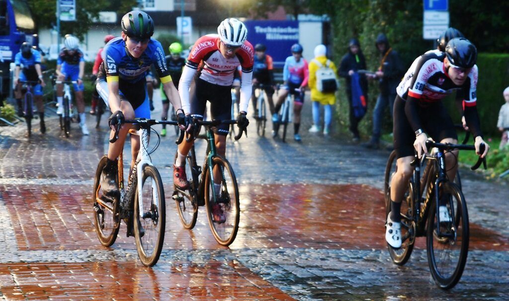Radsportler auf Crossrädern fahren über nasses Pflaster