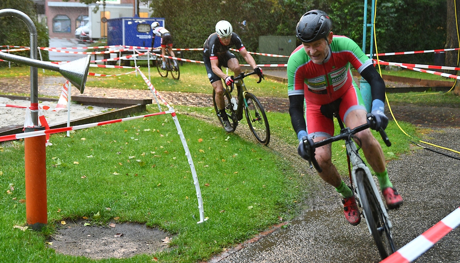 Crossfahrer fahren bei Regen durch eine mit Flatterband abgesperrte Kurve auf Rasen