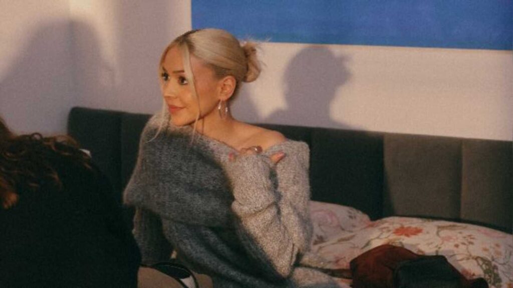 Sängerin AYLIVA mit hochgesteckten blonden Haaren und grauem Strickpullover