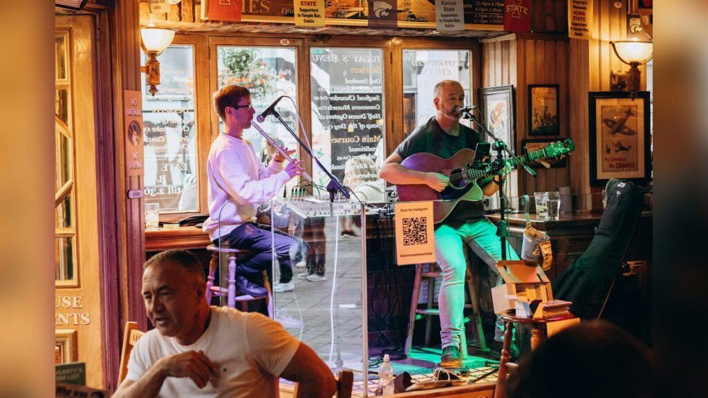 Zwei Musiker spielen Gitarre und Blasinstrument in einem Pub (Symbolbild)