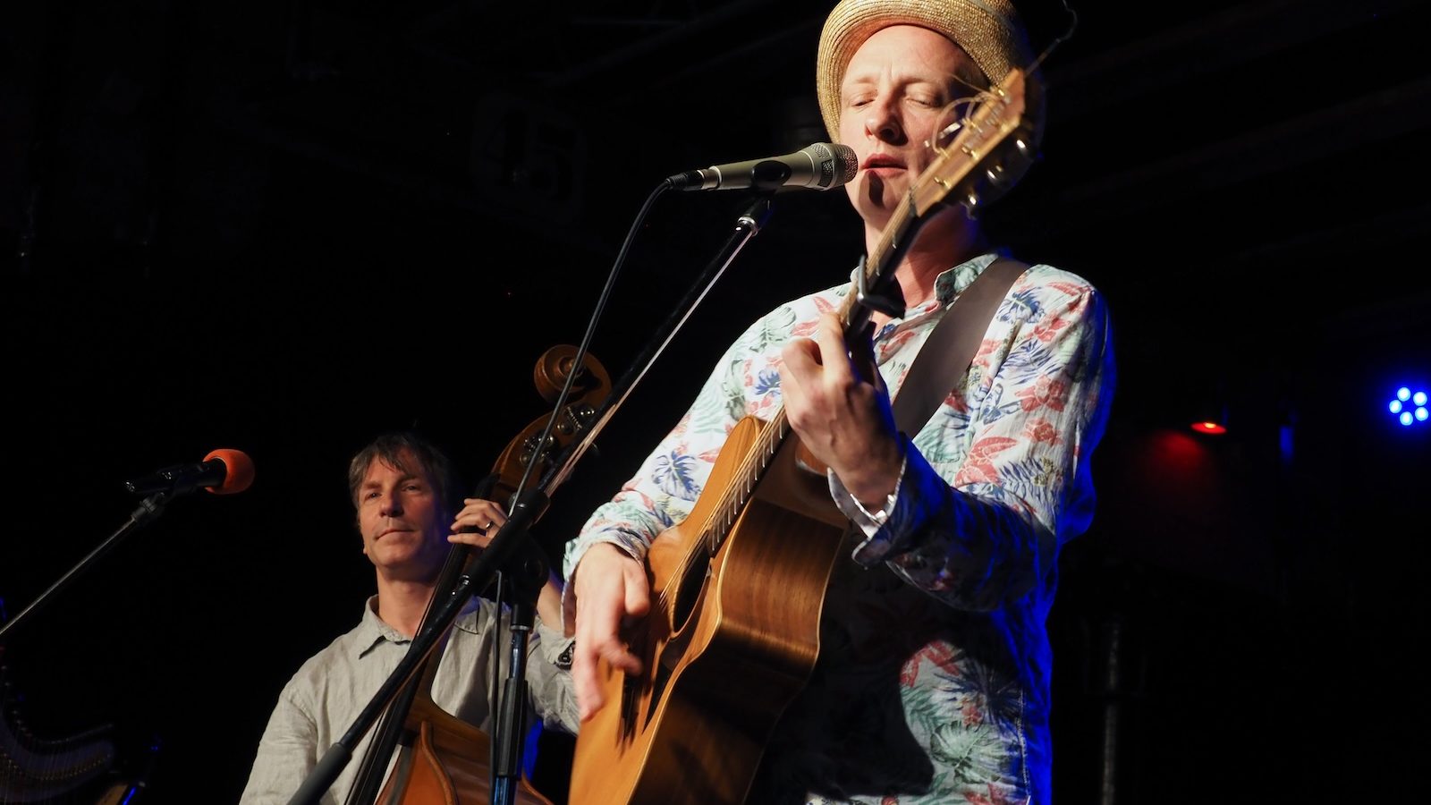 Toni Geiling mit Strohhut singt und spielt Gitarre, dahinter ein Kontrabassist auf der Bühne