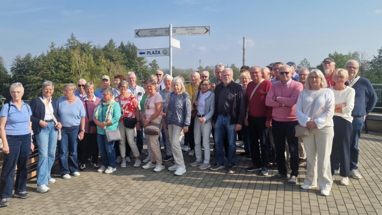 Gruppenfoto der Lingener Reisegruppe im Freien an einem Wegweiser mit Richtungsschildern nach Lingen und Hronov