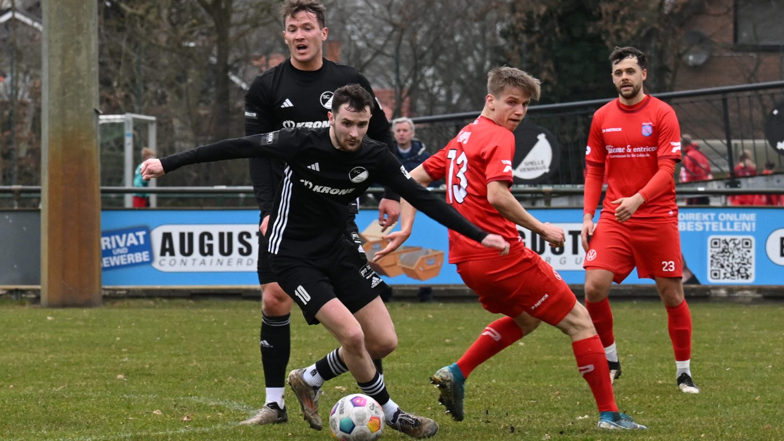 Fußballspieler in schwarzer und roter Ausrüstung während eines Spiels auf dem Platz.