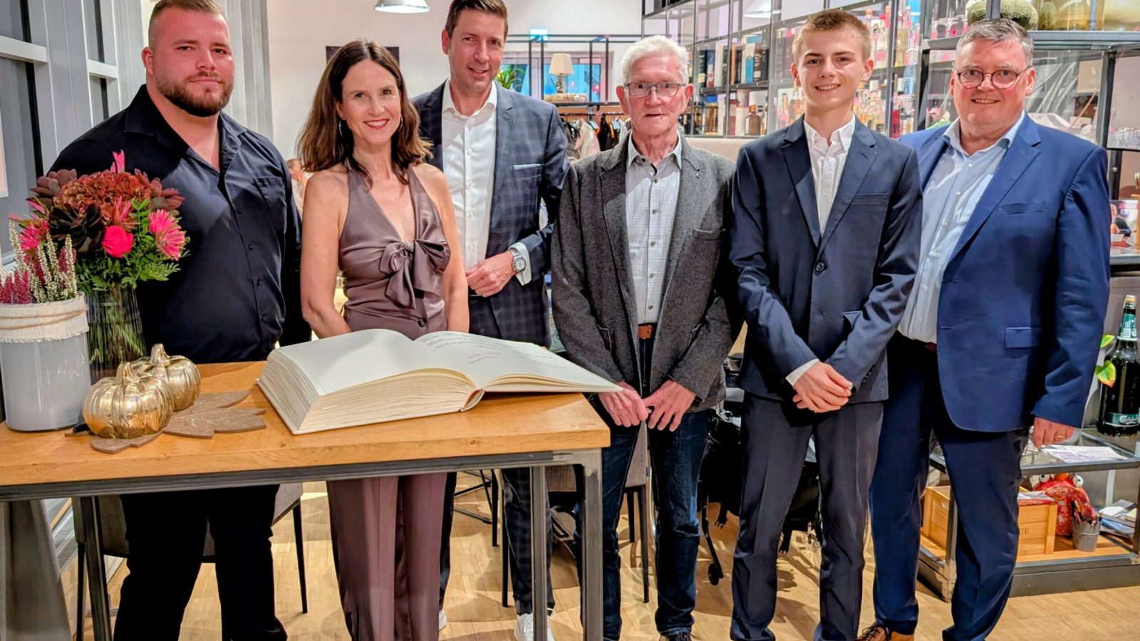 Sechs Personen posieren für ein Gruppenfoto in einem Innenraum mit einem großen Buch auf einem Tisch.