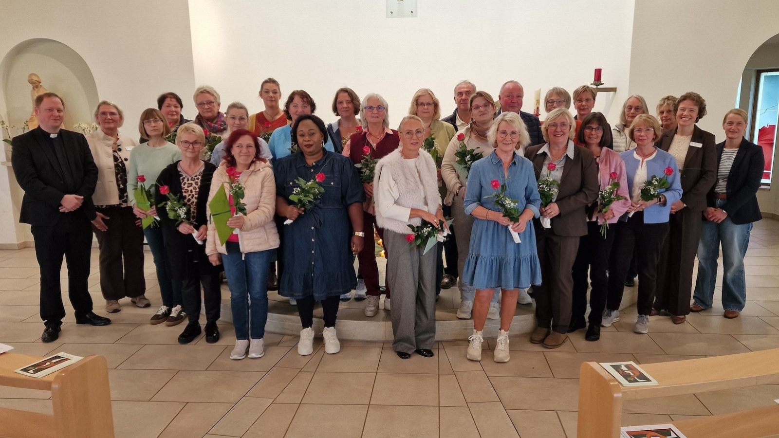 Gruppenfoto der Jubilarinnen und Jubilare mit roten Rosen in einer Kapelle, links Propst Christoph Schwerhoff