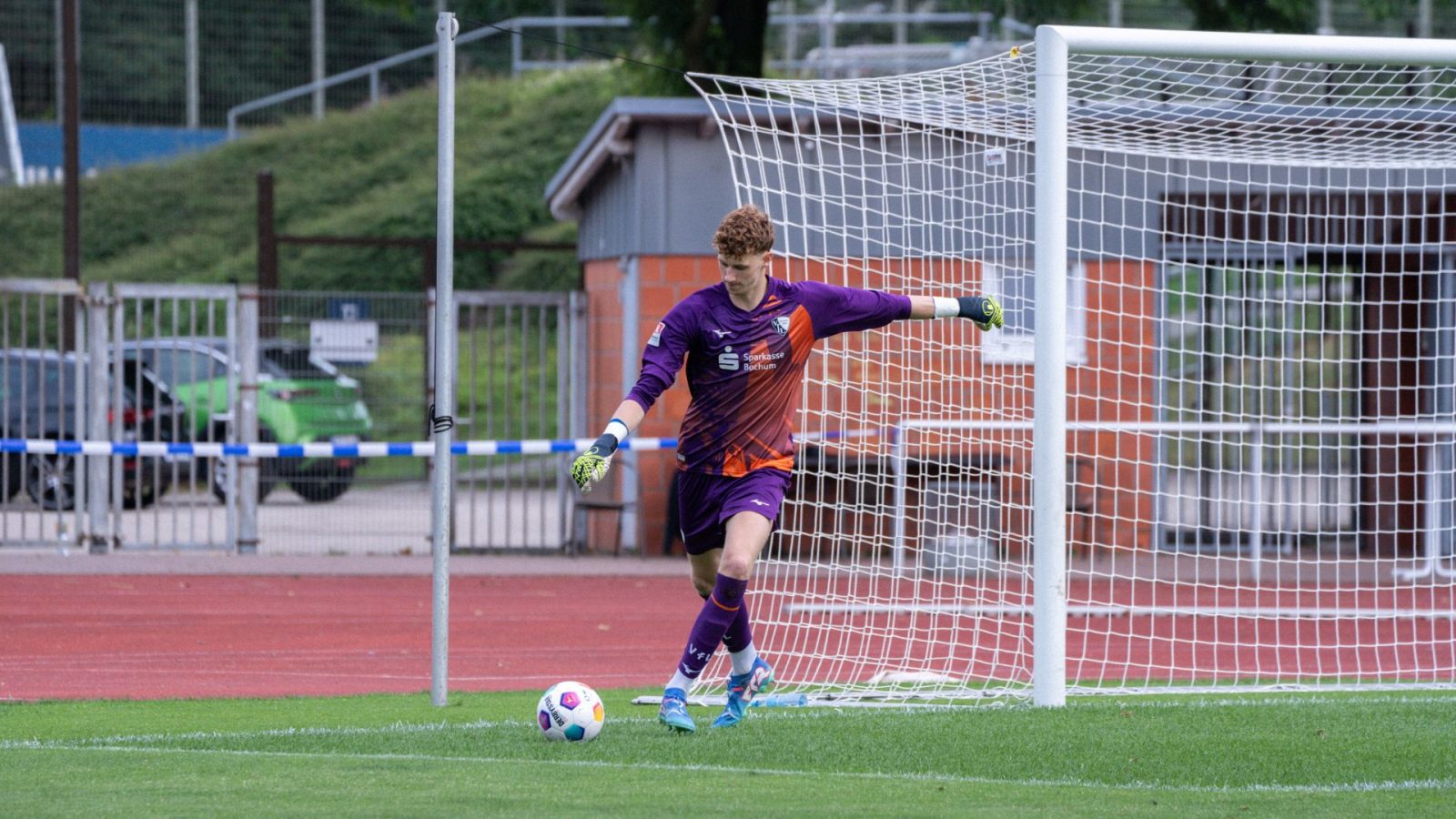 Ein Torwart in lila Trikot kickt den Ball im Fußballspiel, bereit für den Abstoß im Stadion.